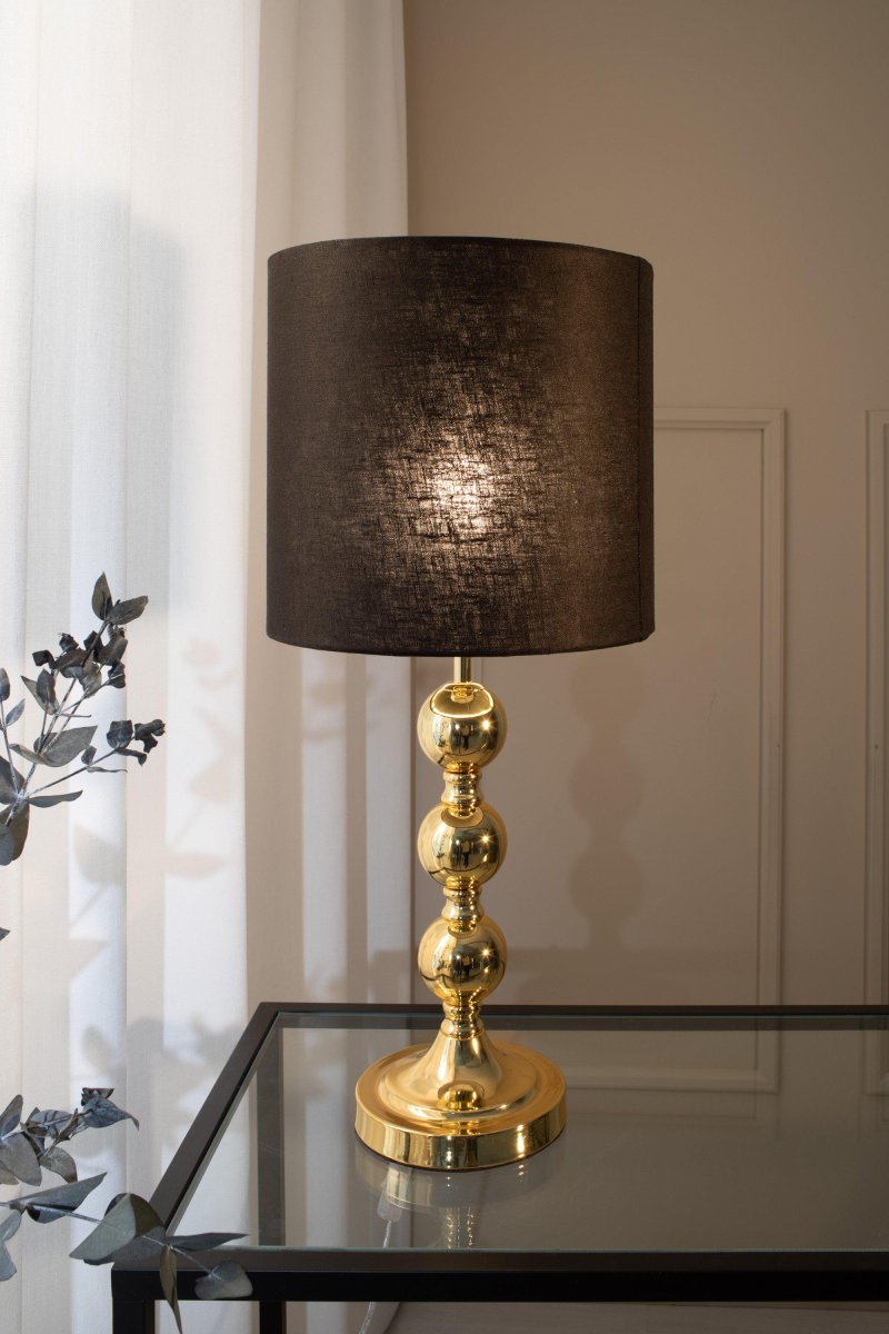 Octo 57cm Messinki pöytävalaisin valmistajalta Markslöjd - Octo on tyylik&auml;s p&ouml;yt&auml;valaisin, jossa on musta pellavavarjostin ja messinginv&auml;rinen lampunjalka kolmen pehme&auml;n py&ouml;re&auml;n pallon muodossa.