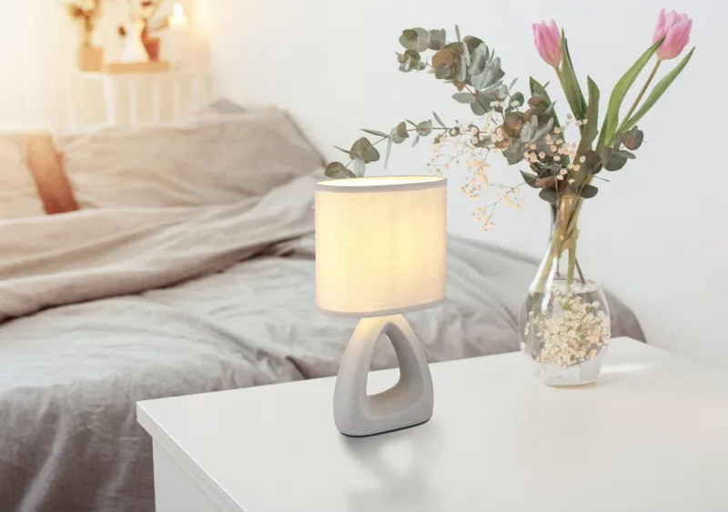 Triangle 30cm Harmaa pöytävalaisin valmistajalta Globo Lighting - Den triangelformade basen med ett stilrent utskuret h&aring;l ger ett modernt intryck, medan den ovala textilsk&auml;rmen i gr&aring; f&auml;rg sprider ett behagligt och j&auml;mnt ljus.