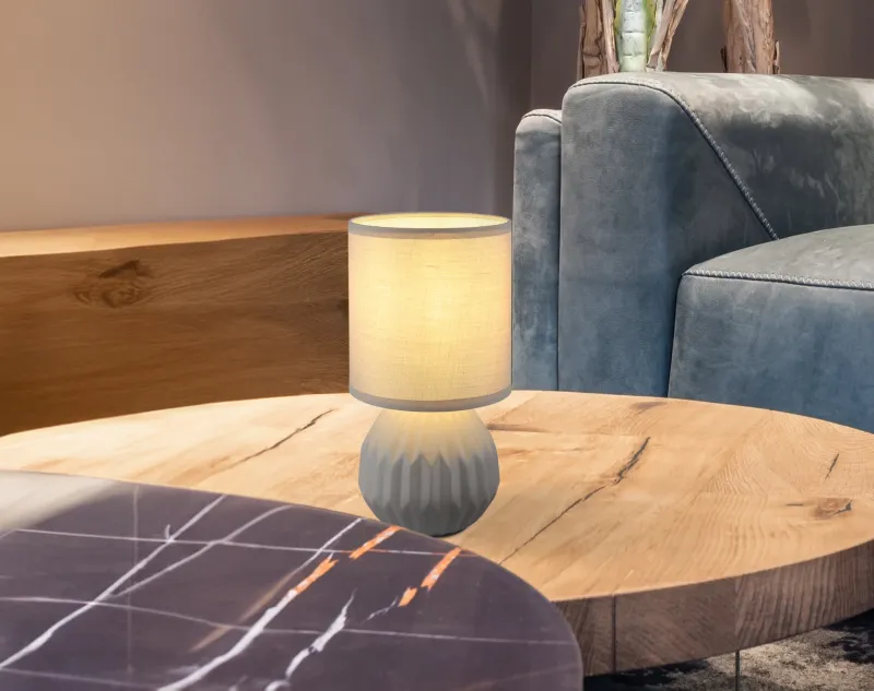 Sylas 23cm Harmaa pöytävalaisin valmistajalta Globo Lighting - Den rundade keramiska basen i elegant gr&aring;tt och den matchande cylindriska textilsk&auml;rmen skapar en harmonisk och modern estetik.