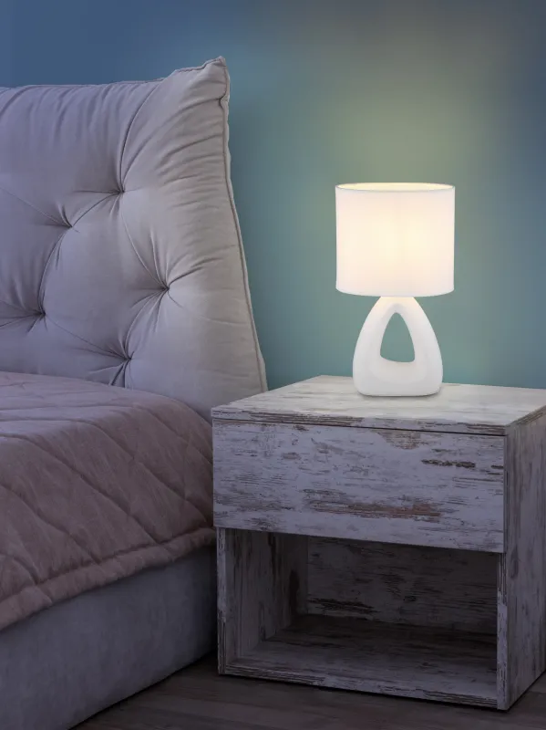 Triangle 30cm Valkoinen pöytävalaisin valmistajalta Globo Lighting - Den triangelformade basen med ett stilrent utskuret h&aring;l ger ett modernt intryck, medan den ovala textilsk&auml;rmen i vit f&auml;rg sprider ett behagligt och j&auml;mnt ljus.