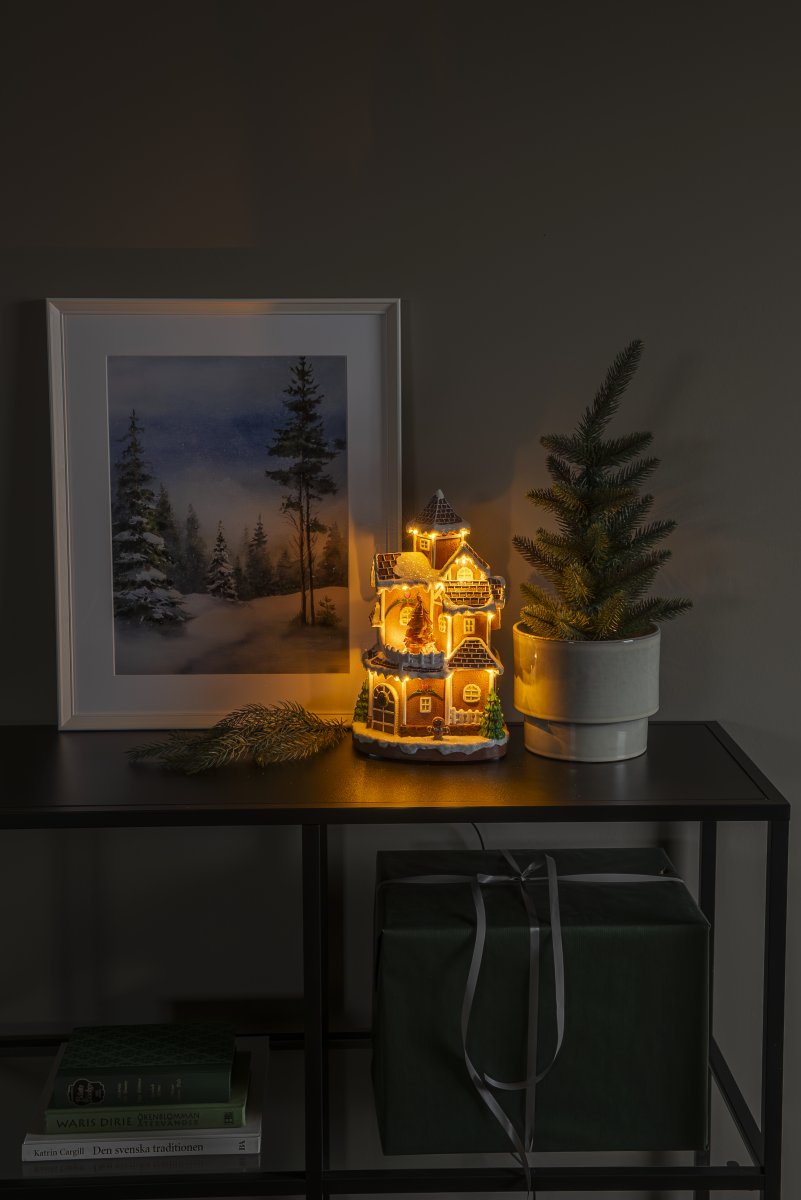 Piparkakkukylä 30cm Ruskea valmistajalta Konstsmide - Yksityiskohtainen talo, jossa on lumen peitt&auml;m&auml; katto, kiilt&auml;v&auml;t ikkunat ja koristeltu kuusi, levitt&auml;&auml; l&auml;mmint&auml; ja kutsuvaa valoa huoneeseen.