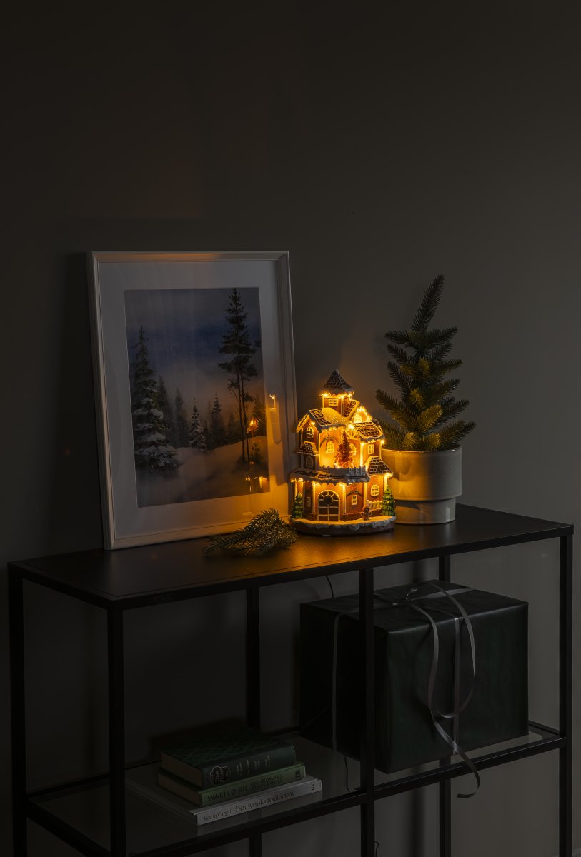 Piparkakkukylä 30cm Ruskea valmistajalta Konstsmide - Yksityiskohtainen talo, jossa on lumen peitt&auml;m&auml; katto, kiilt&auml;v&auml;t ikkunat ja koristeltu kuusi, levitt&auml;&auml; l&auml;mmint&auml; ja kutsuvaa valoa huoneeseen.
