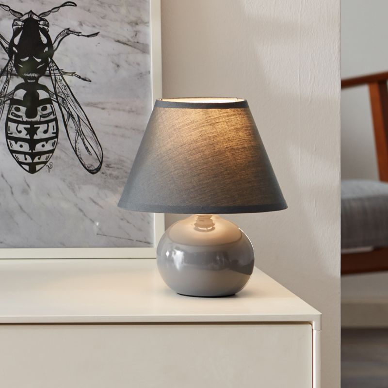 Primo 23cm Tummanharmaa pöytävalaisin valmistajalta Brilliant - Se on valmistettu tekstiilist&auml; ja keramiikasta ja antaa miellytt&auml;v&auml;n valon.